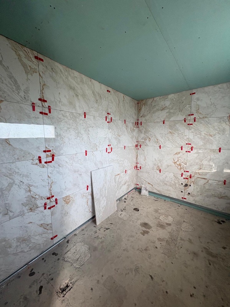 Paredes de casa de banho a ser revestidas com placas de cerâmica de grande formato, com niveladores vermelhos nas juntas