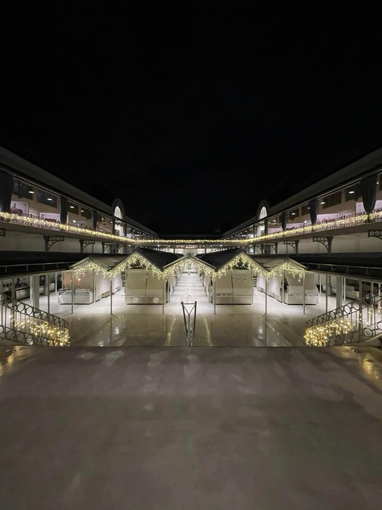 Mercado coberto à noite com bancas e varandins decorados com franjas de luz branca