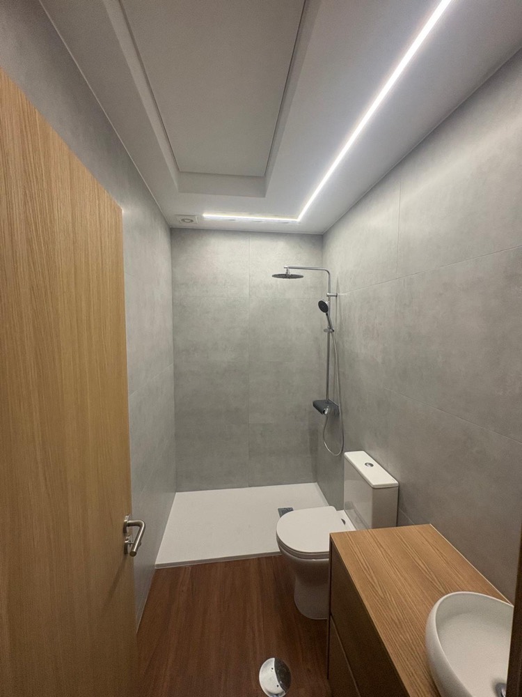 Casa de banho com revestimento cinzento, teto rebaixado com fita LED e base de duche